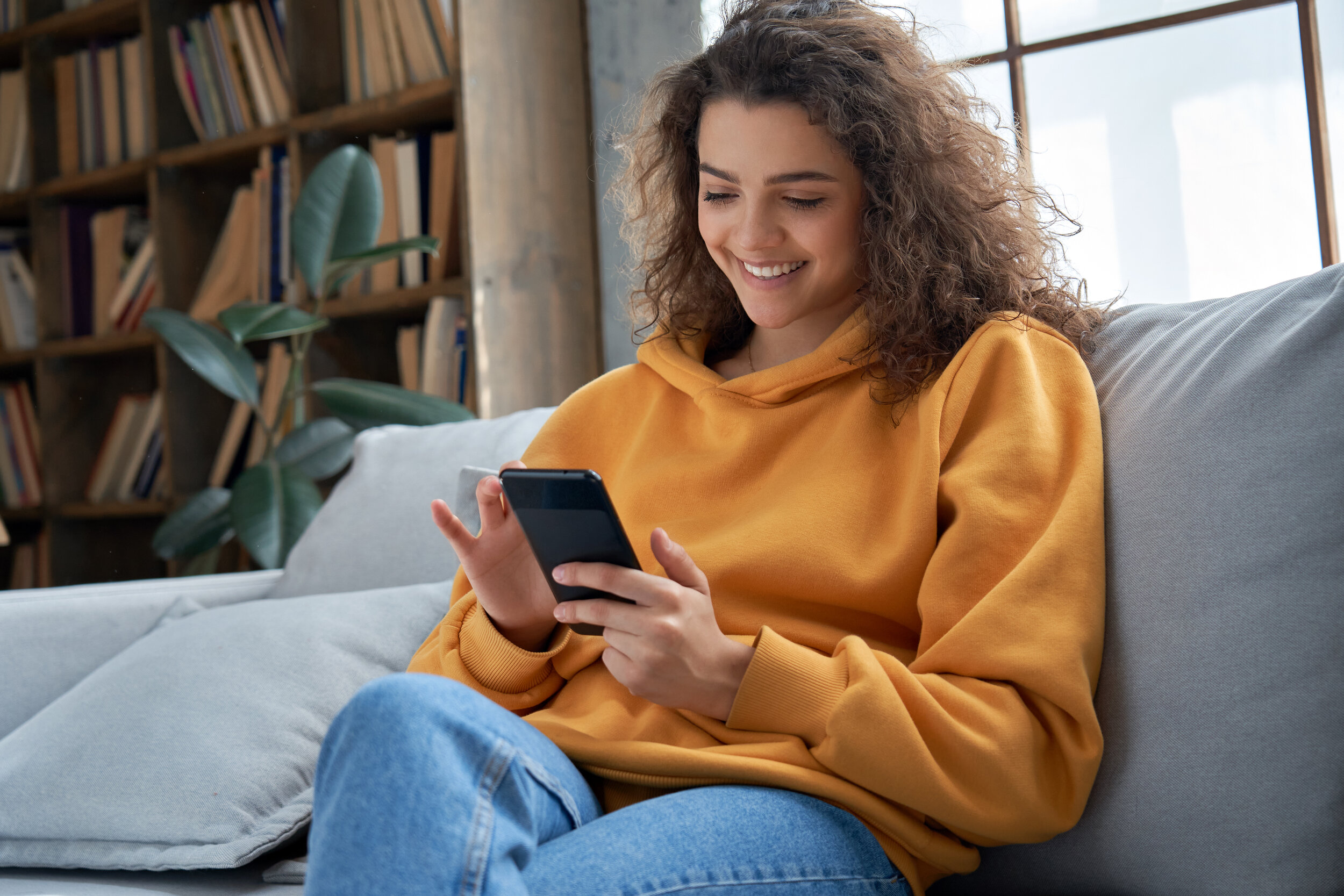 A woman in a yellow sweater using a smart phone.