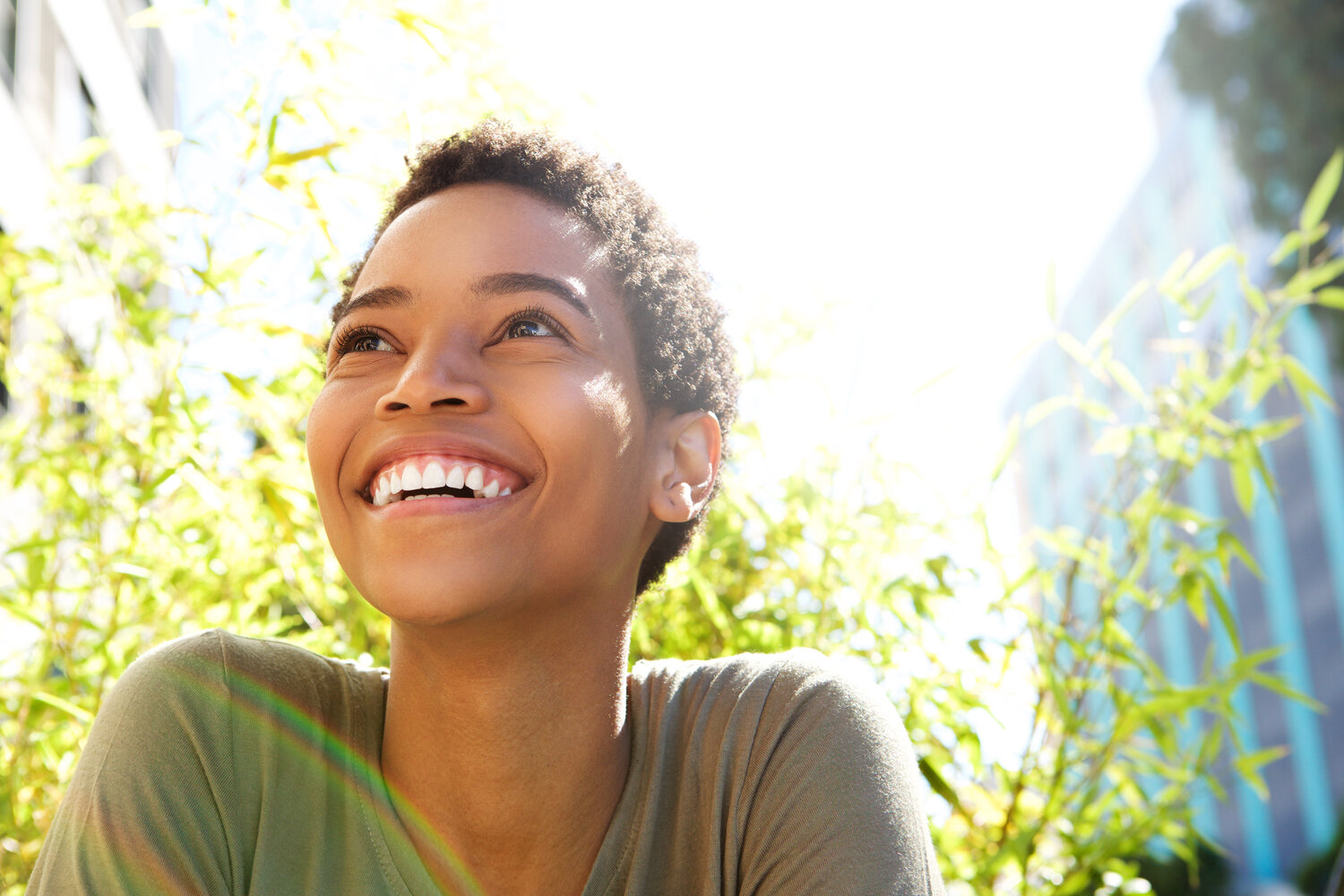 A woman smiling outside in a sunny urban area.