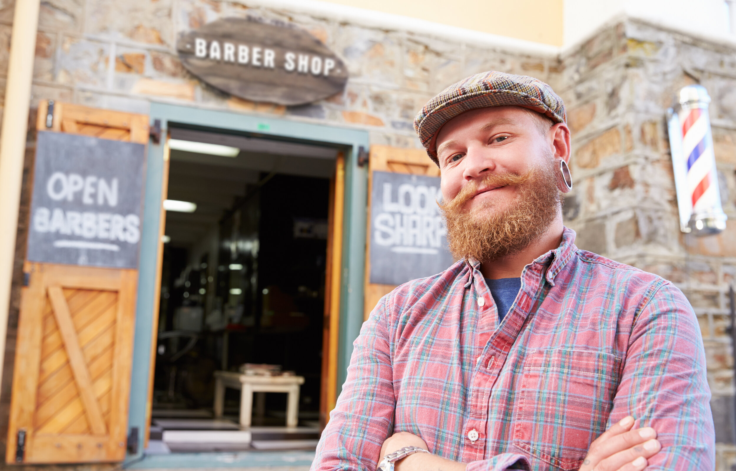 An owner of a barbershop standing outside of the barber shop and smiling.