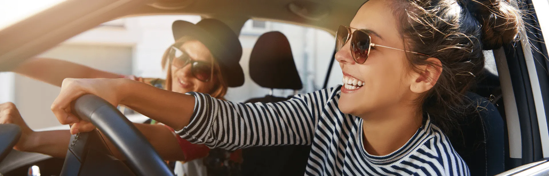 A woman smiling and driving a car with a person in the passenger seat.