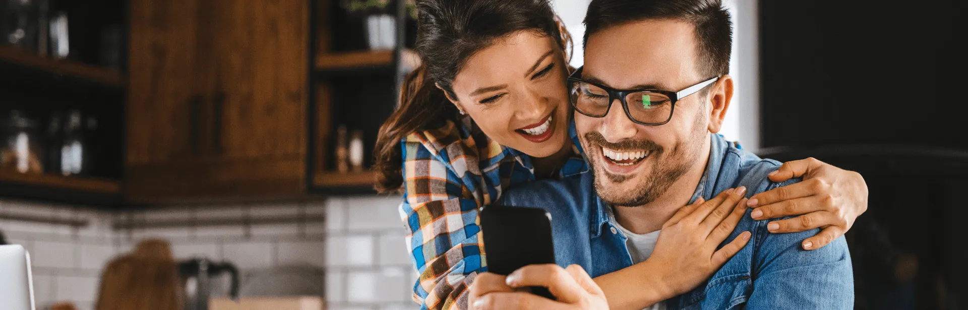Two people looking at a phone screen while in a kitchen.