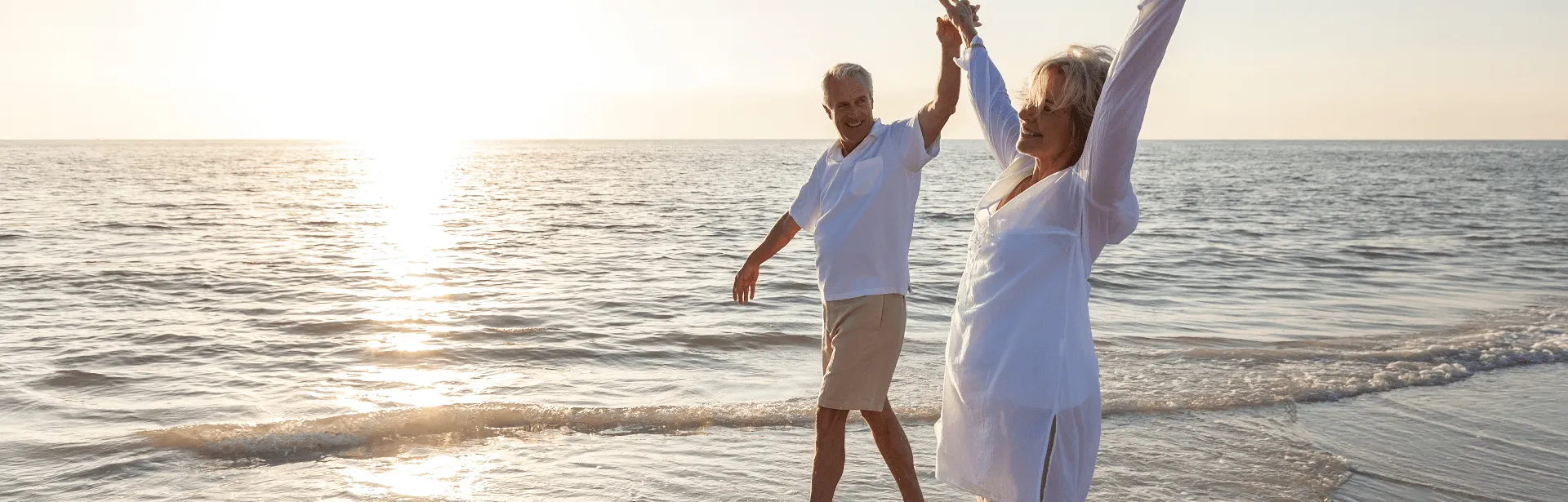 A couple walking down the beach with waves in the background.